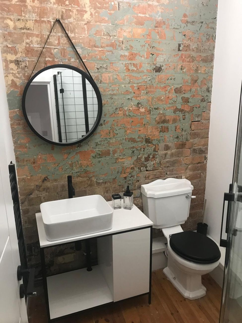 Exposed brick feature wall bathroom with round mirror and wall-hung basin